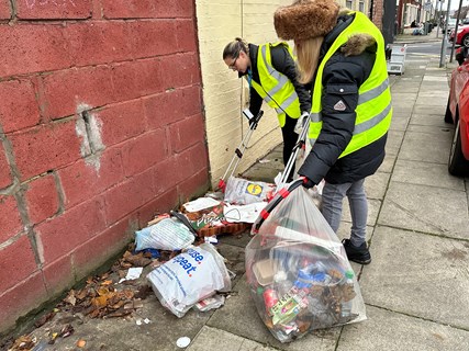People picking up litter from the streets, including plastic bags and takeaway boxes.