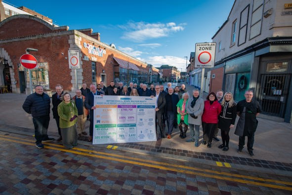 A photo of a banner that includes social value numbers, and a large crowd surrounding. The crowd include Cllrs, local business owners, council officers, staff from WSP and Balfour Beatty