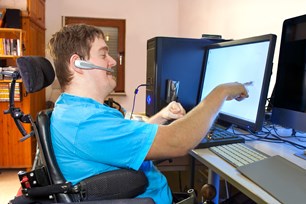 A person in a wheelchair, pointing at a computer screen.