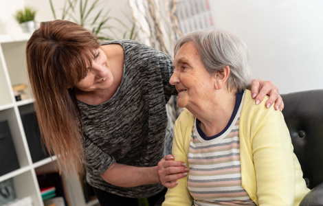 Adult gently supporting an older person while sitting together indoors in a home setting.