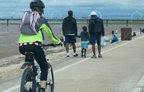 An image of a cyclist and pedestrians walking down alongside the beach, on a marked path. Southport pier is in the background. 