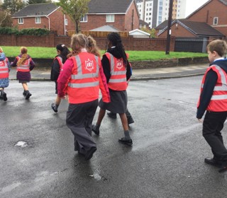 A photo of school children in pink high vis crossing a road