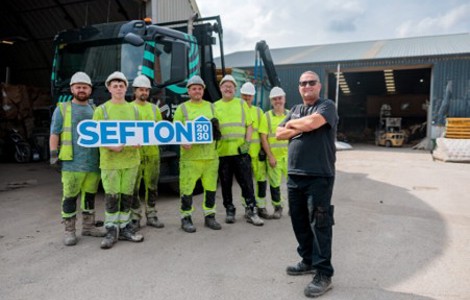 A group of seven workers in high-visibility clothing stand in front of a truck. Six hold a sign that reads SEFTON 2030.