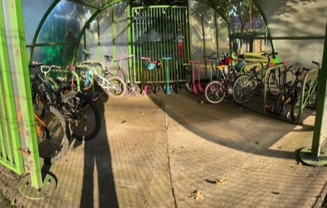 A photo of a bike shelter full with bikes and scooters