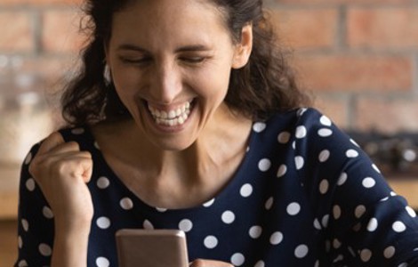 Person looking at a smartphone and raising a clenched fist while sitting at a table indoors.