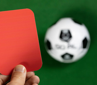 Hand holding red card football in background