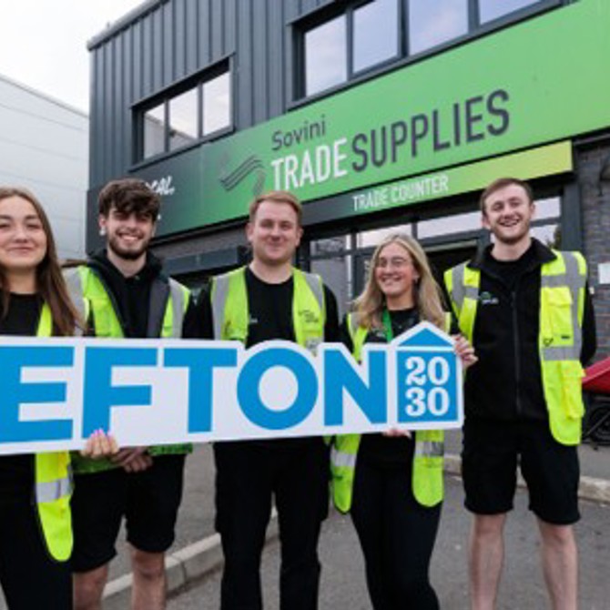 Five people in high-visibility vests hold a sign that says SEFTON 2030 in front of Sovini Trade Supplies.